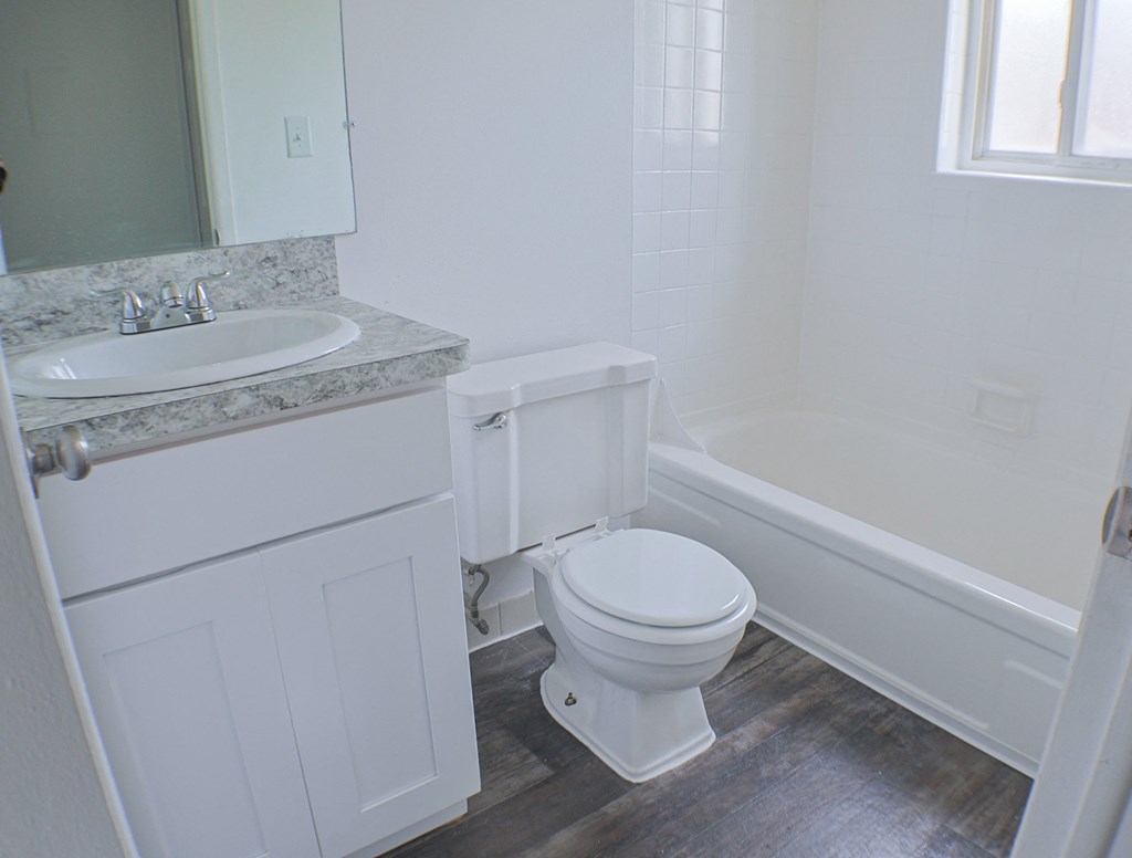 A white toilet sits in a bathroom next to a sink and bathtub.