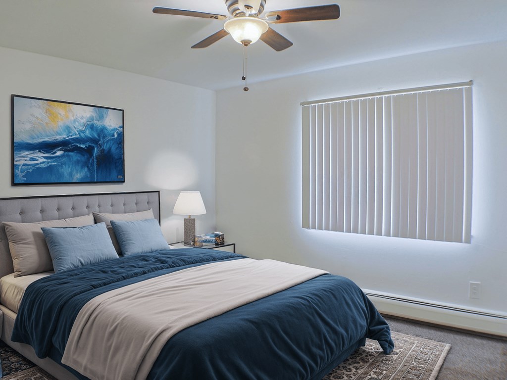 A bedroom with a bed, a ceiling fan, and a painting on the wall.