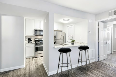 A kitchen with white cabinets and a bar area with black stools.