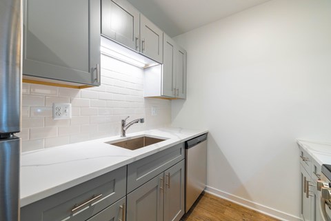 A kitchen with a white counter top and grey cabinets.