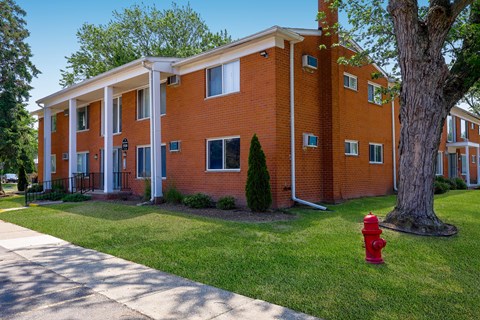 A red fire hydrant sits on a green lawn in front of a red brick building.