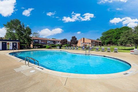 A large outdoor swimming pool surrounded by a concrete deck and lounge chairs.