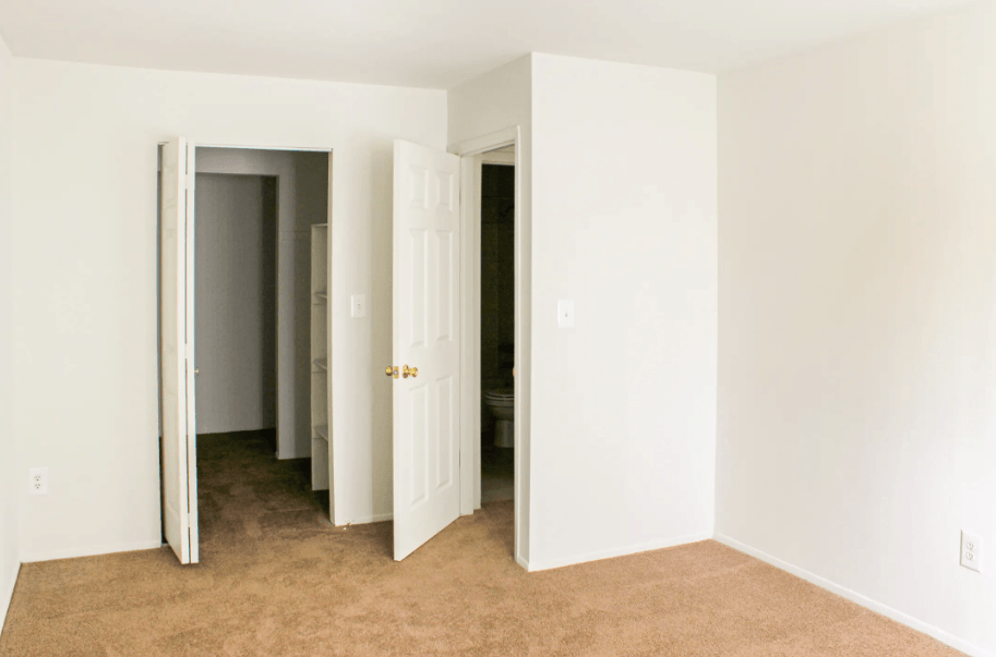 A room with white walls and carpeted floor with two open doors.
