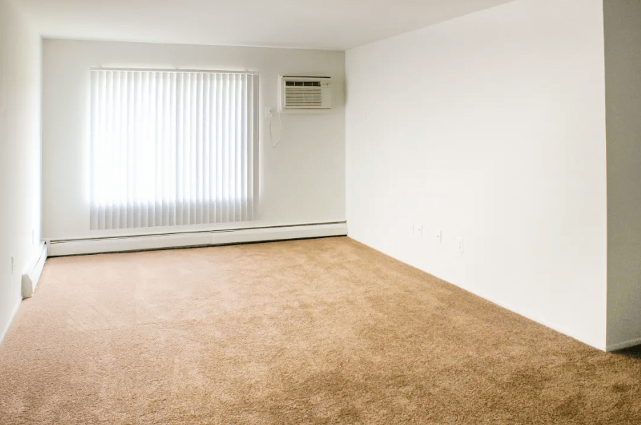 A carpeted room with a window and air conditioner.