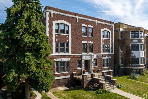 A brown building with a white trim and a green tree in front.