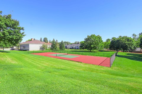 A tennis court is located in a grassy area.