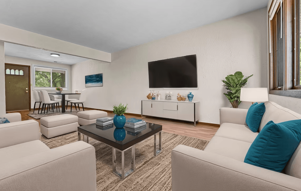A living room with a white couch, a glass coffee table, and a flat-screen TV mounted on the wall.