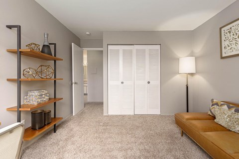 A living room with a couch, a chair, a shelf with decorative items, and a door.