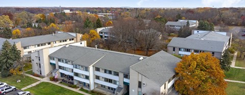A large building with a grey roof is surrounded by trees with orange leaves.