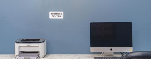 A business center sign is on a wall above a printer and a computer monitor.