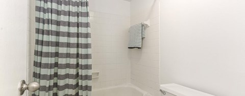 A white bathroom with a shower curtain and a towel hanging on the wall.
