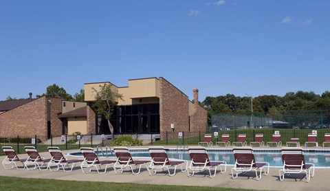 A poolside with chairs and a building in the background.