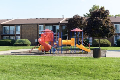 A playground with a red slide and yellow slide in front of a building.