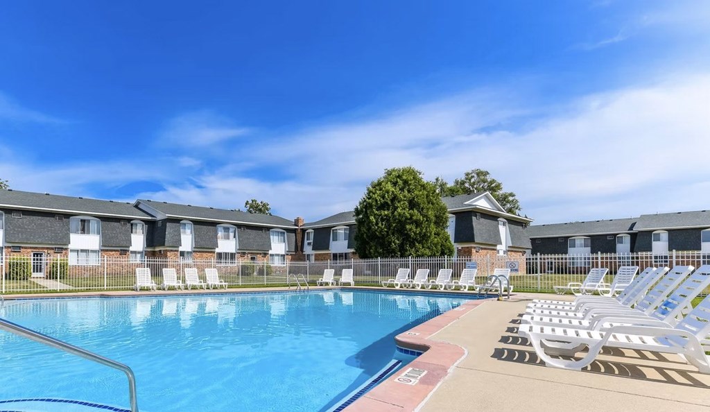 A swimming pool surrounded by sun loungers and apartment buildings.