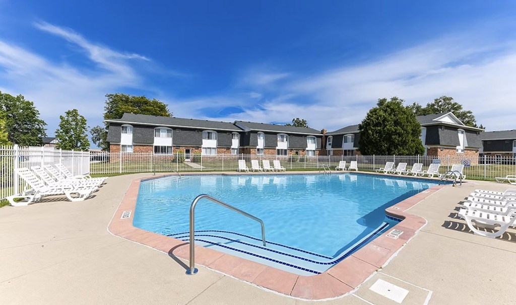 A swimming pool surrounded by chairs and a fence with houses in the background.