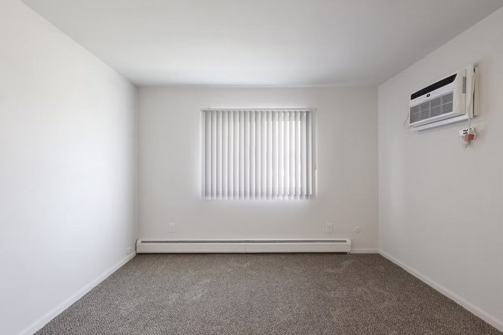 A room with a window covered by blinds and an air conditioner on the wall.