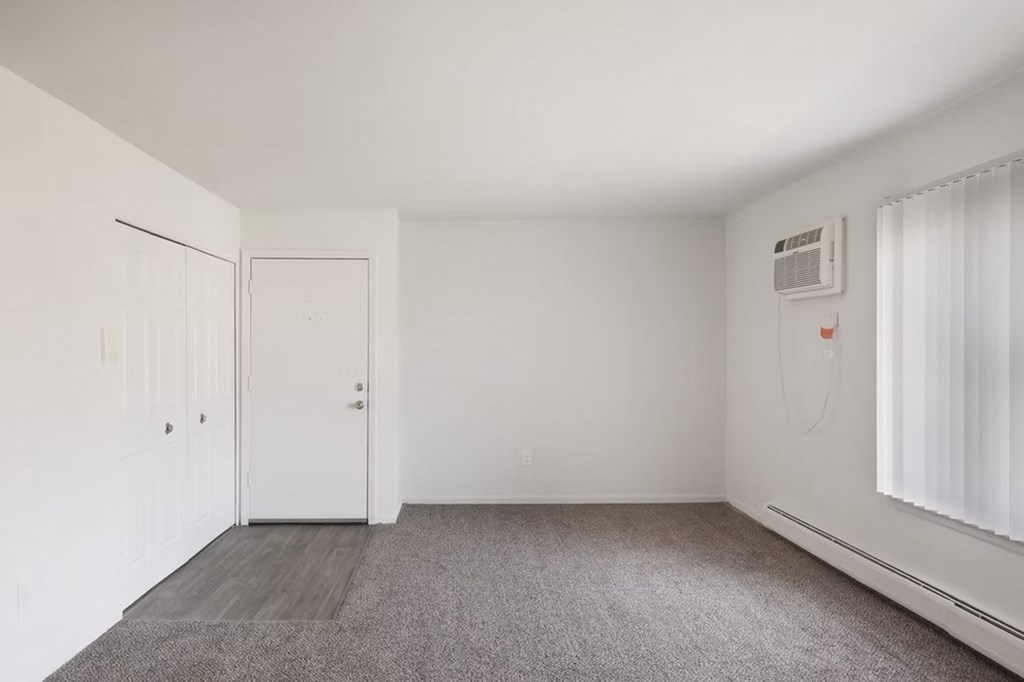 A room with a carpeted floor, a window with white curtains, and a white door.
