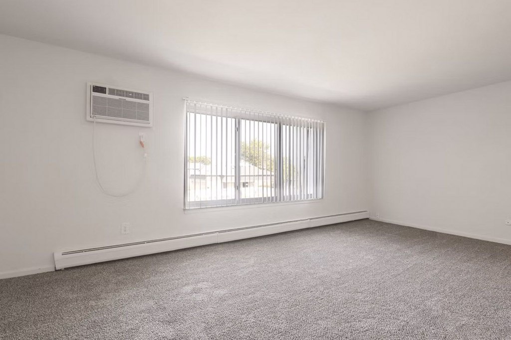 A room with a window covered by blinds and an air conditioner on the wall.