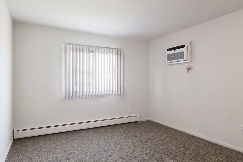 A room with a window covered by blinds and an air conditioner mounted on the wall.