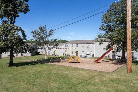 A playground with a slide and swings in a grassy area.