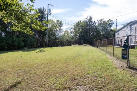 A grassy field with a fence on one side and trees on the other.