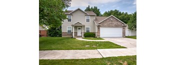 A two-story house with a garage is surrounded by a green lawn.