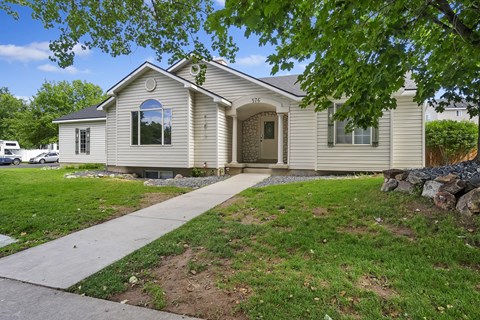 A house with a white exterior and a brown door is surrounded by a grassy area and trees.