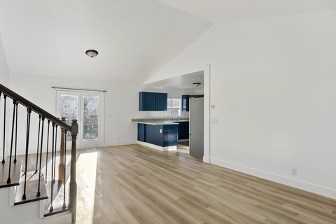 A spacious room with wooden floors and a staircase on the left side.