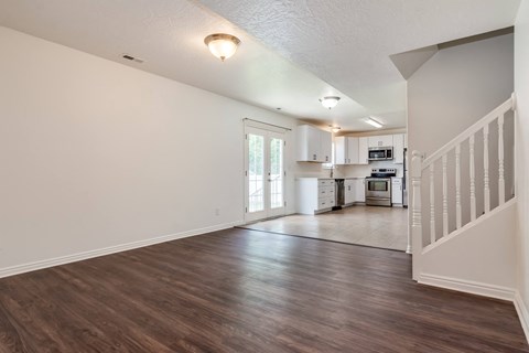 A spacious living room with hardwood floors and a staircase on the right.