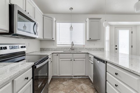A kitchen with white cabinets and a marble countertop.
