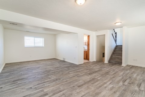 A spacious room with wooden flooring and a staircase.