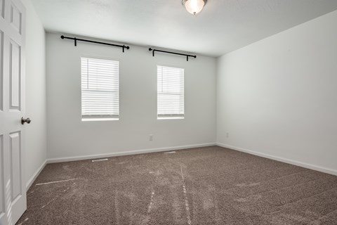 A room with a carpeted floor and two windows with blinds.