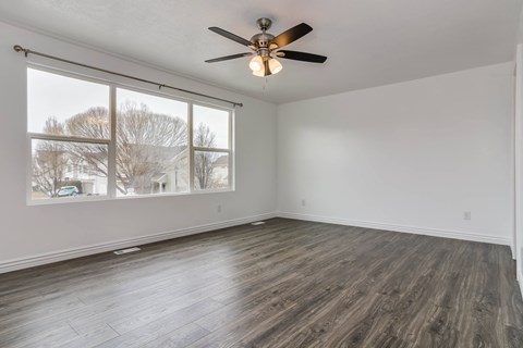 A room with a ceiling fan and a window with a view of trees and houses outside.