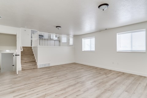 A spacious room with wooden floors and a staircase leading to another level.