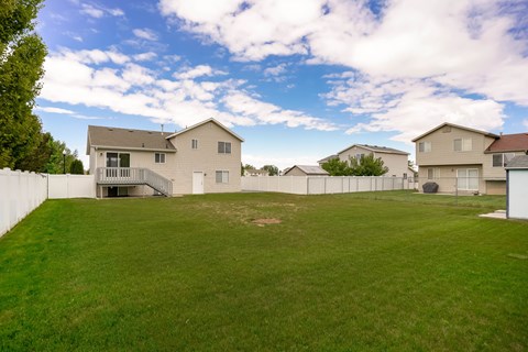 A backyard with a large grassy area and a few houses in the background.