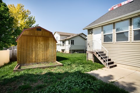 A wooden shed sits in a grassy yard next to a house.