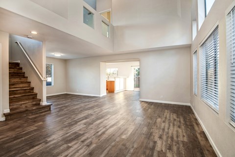 A spacious room with wooden flooring and a staircase on the left side.