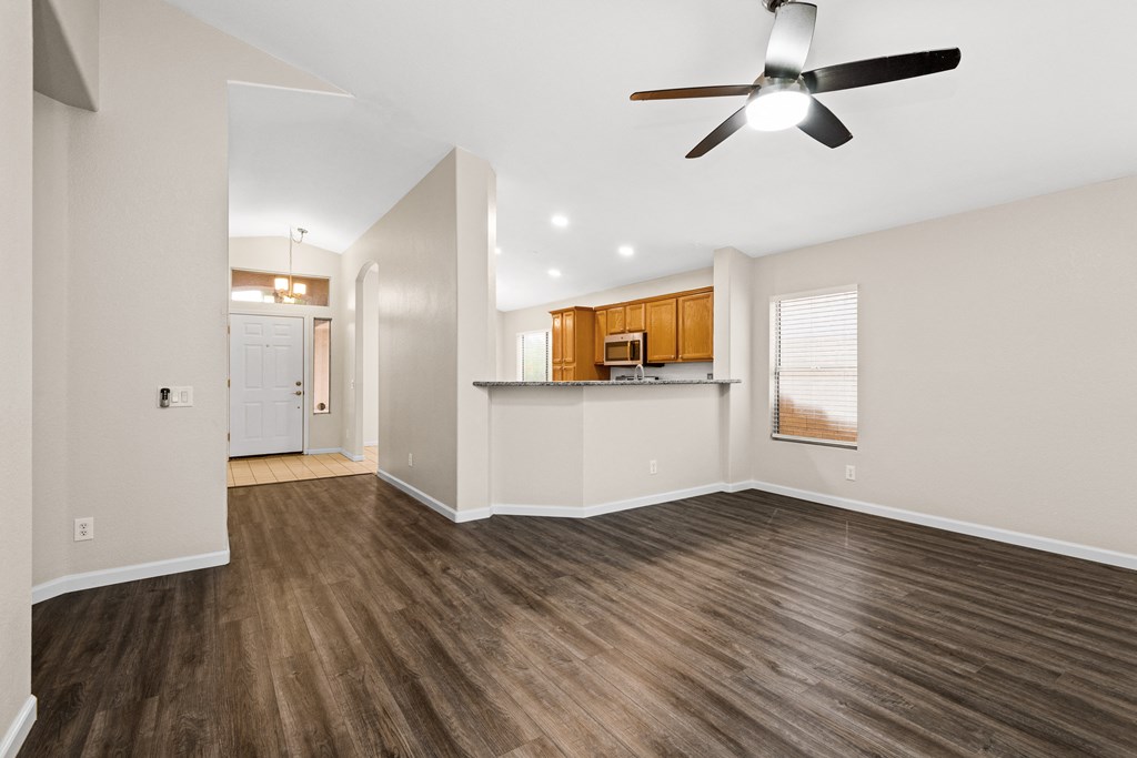 an empty living room with a ceiling fan and a kitchen