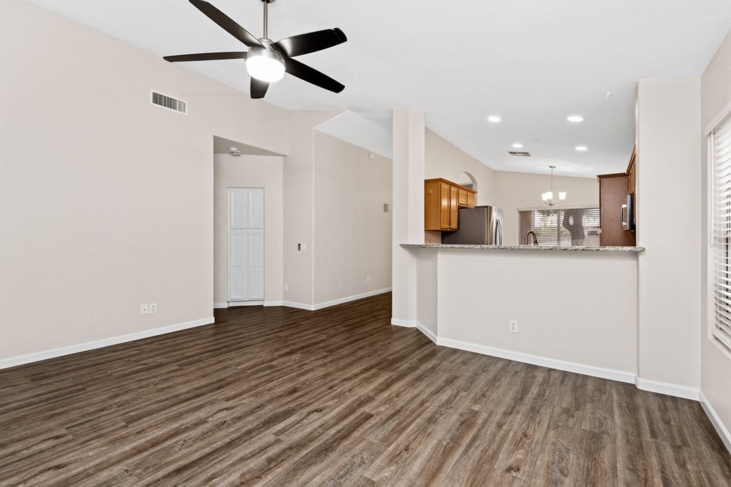 an empty living room with a ceiling fan and a kitchen