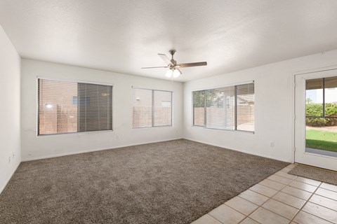 an empty living room with a ceiling fan and windows