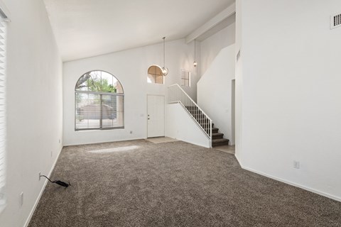 A spacious room with a staircase and a window with blinds.