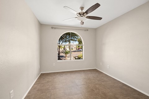an empty living room with a large window and a ceiling fan