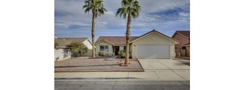 A house with a red tile roof and a white garage door is surrounded by palm trees.
