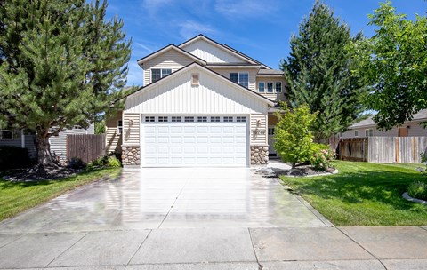 A two-story house with a garage is surrounded by a fence and trees.
