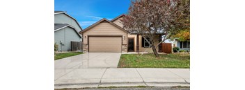 A house with a brown garage door is surrounded by a sidewalk and a tree with red leaves.