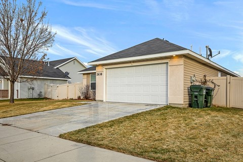 A house with a white garage door and a green trash bin in front.