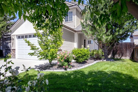 A house with a white garage door and a tree in front of it.