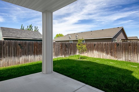 A white pillar stands in a concrete patio with a wooden fence and houses in the background.