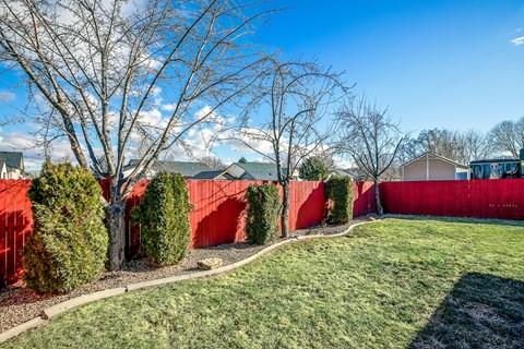 A red fence surrounds a green lawn with trees.