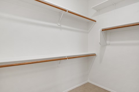 a walk in closet with a white wall and a wooden shelf